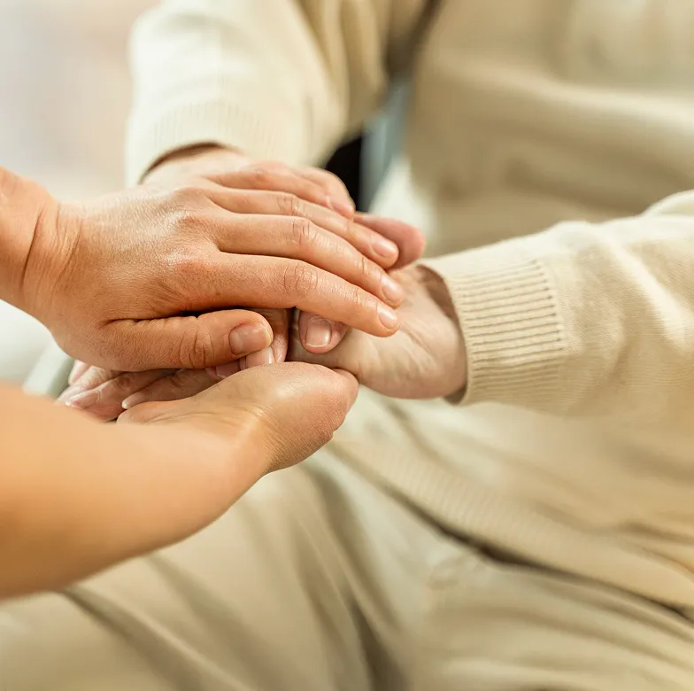 Astar Homecare end of life care: caregiver holding an elderly person’s hands in a comforting home environment