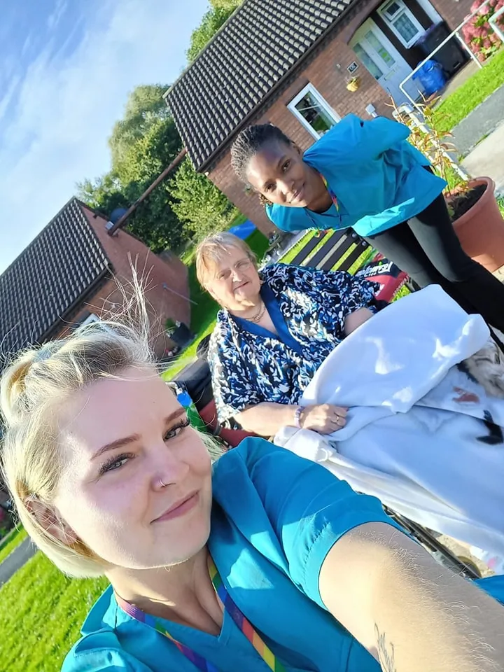 Astar Homecare carers and a female client in a wheelchair enjoying the sunshine outside residential housing.