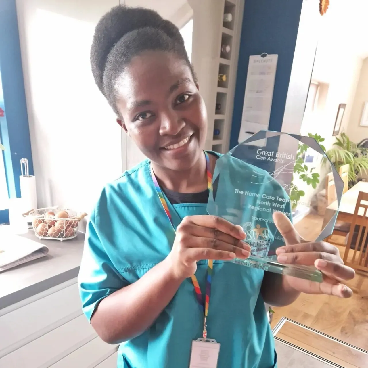 Astar Homecare carer proudly holding a regional Great British Care Award trophy in a kitchen environment.
