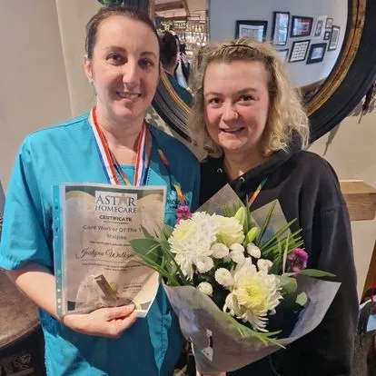 Astar Homecare carer receiving a Care Worker of the Month certificate, standing next to a colleague with flowers.