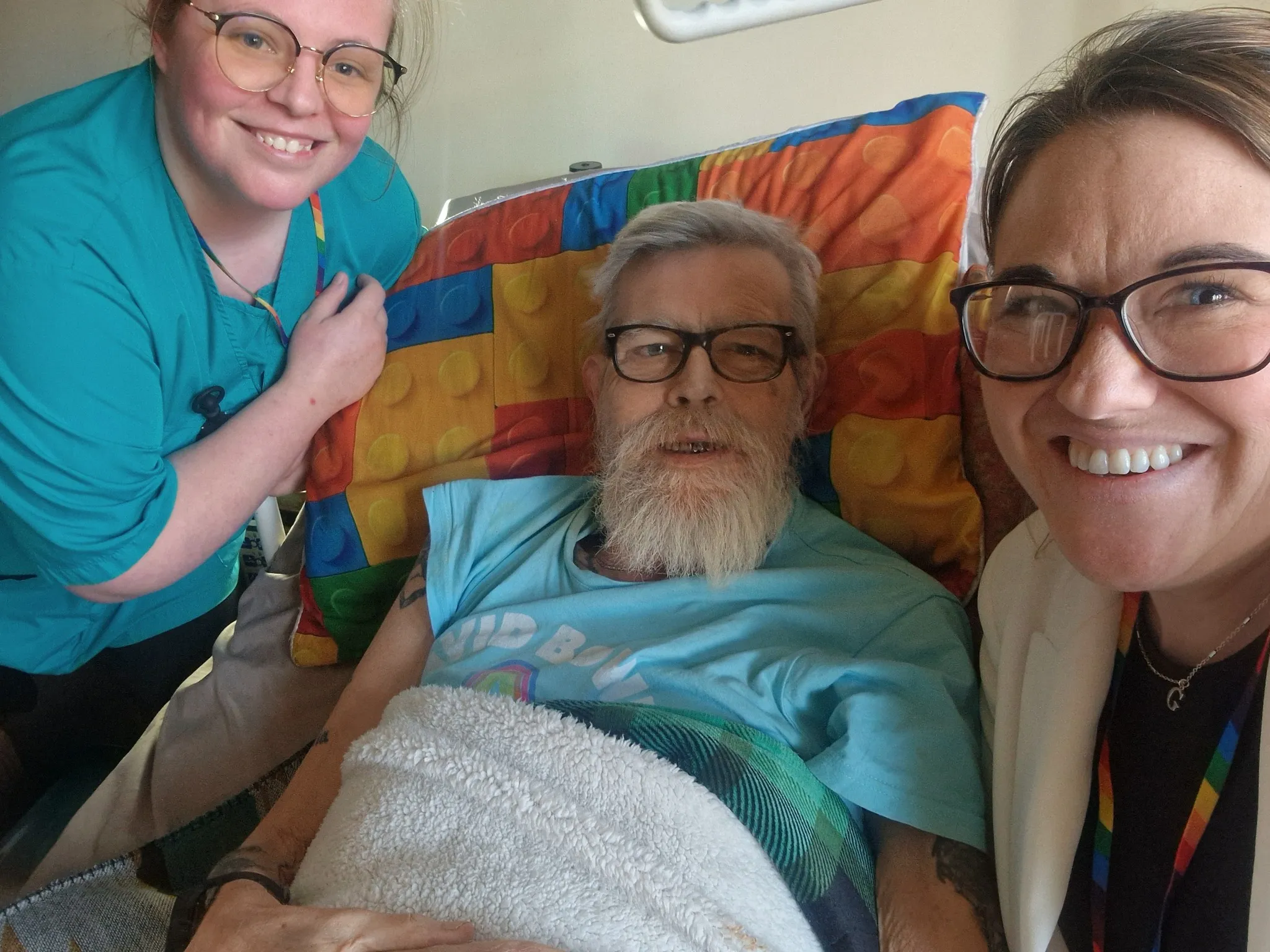 Astar Homecare carers visiting an elderly male client in bed, smiling together for a warm and caring selfie.