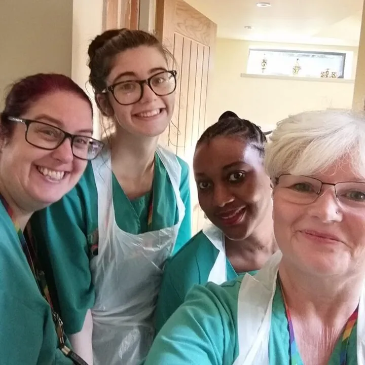Four Astar Homecare carers wearing uniforms and aprons, smiling while working in a client’s home.