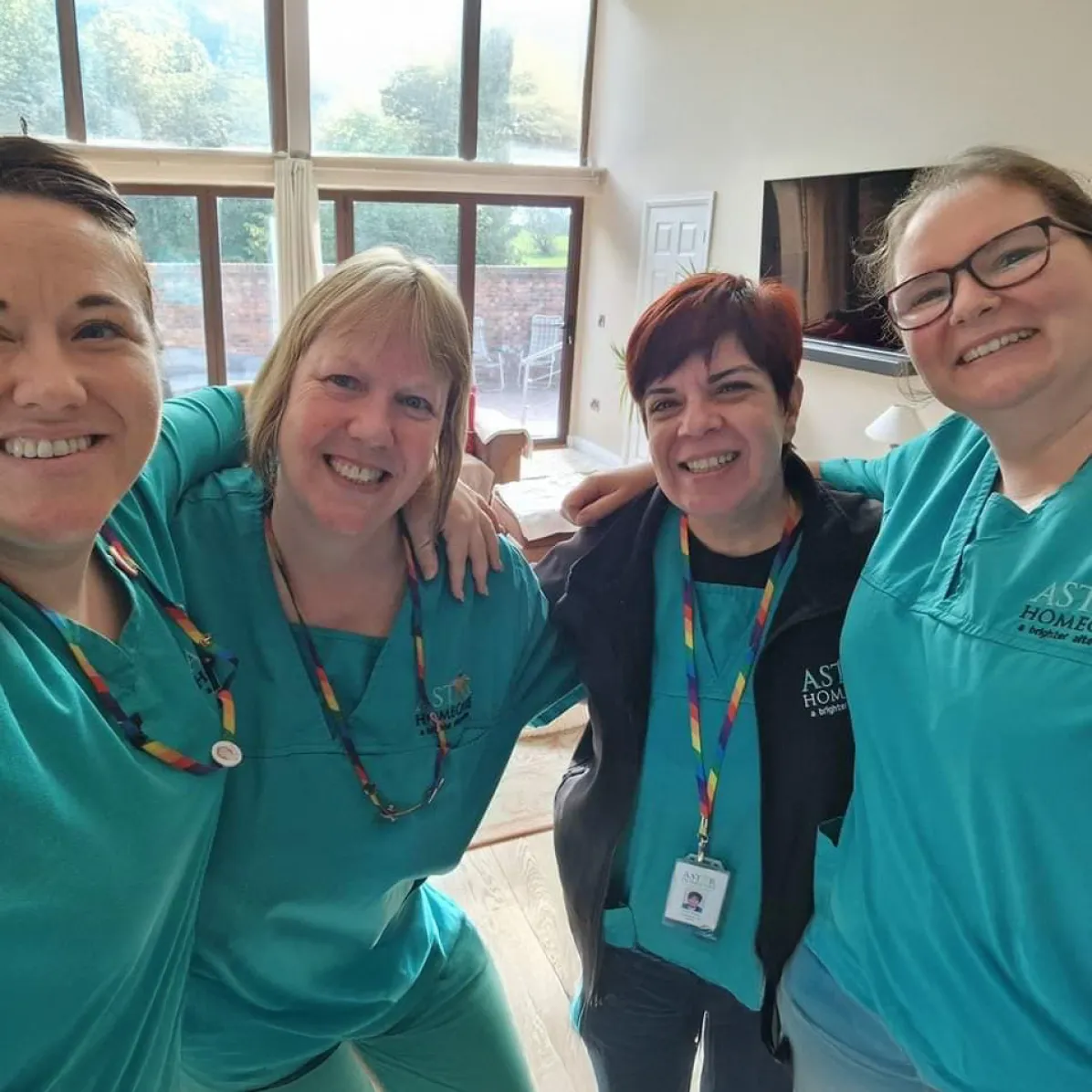 Four smiling Astar Homecare team members posing together indoors, wearing uniforms and lanyards in a bright, welcoming room.